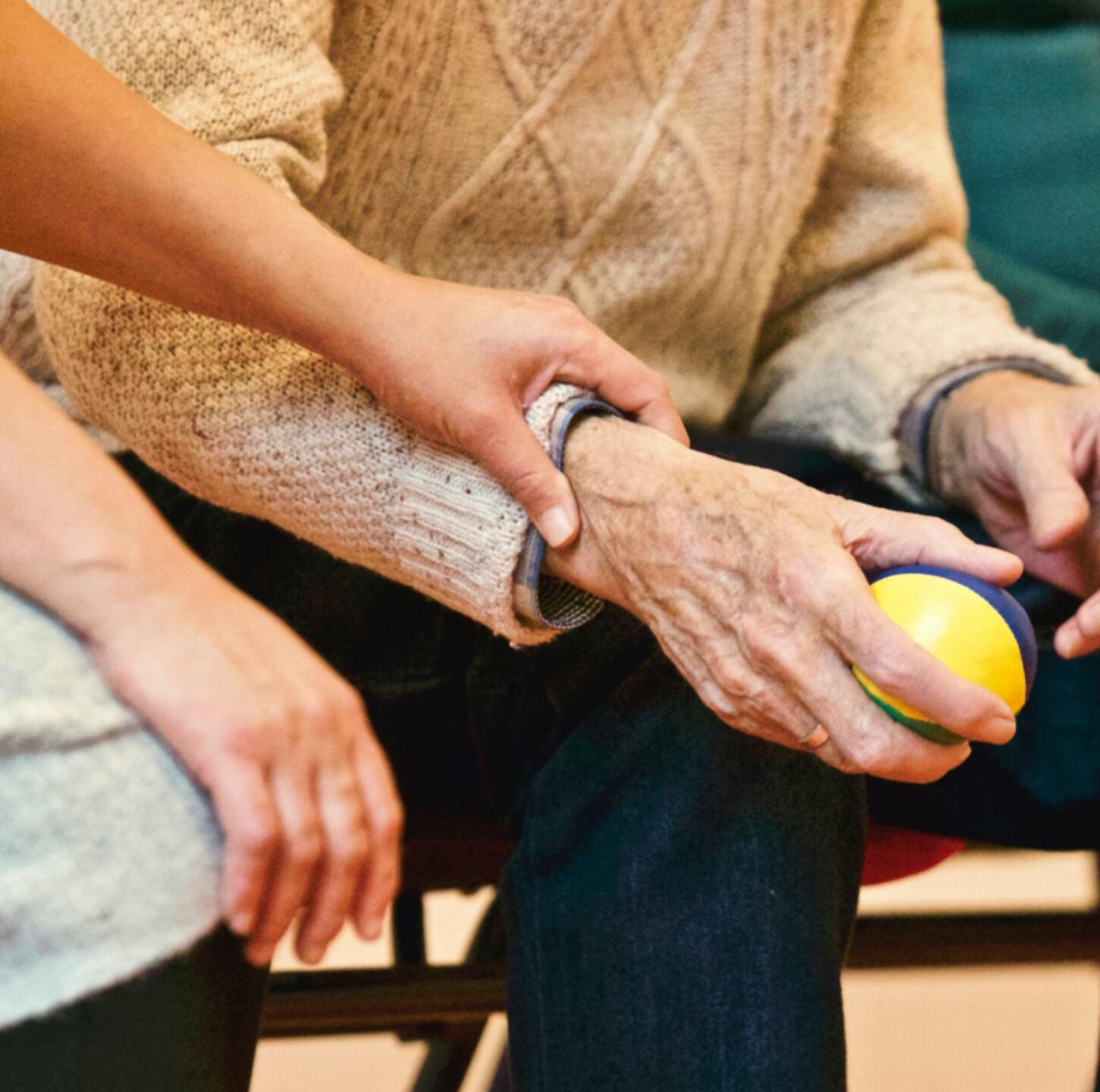 An elderly person receives support from a caregiver, holding hands indoors, showcasing compassion.